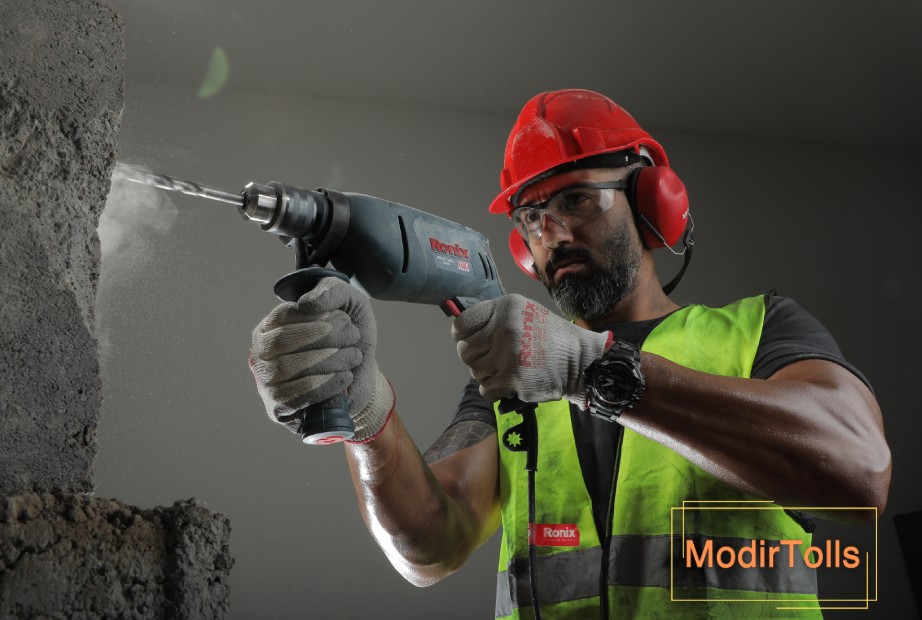 فردی با پوشش ایمنی در حال سوراخ کردن دیوار بتنی با دریل برقی